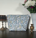 Floral-patterned pouch on a wooden surface with decorative items and flowers in the background.