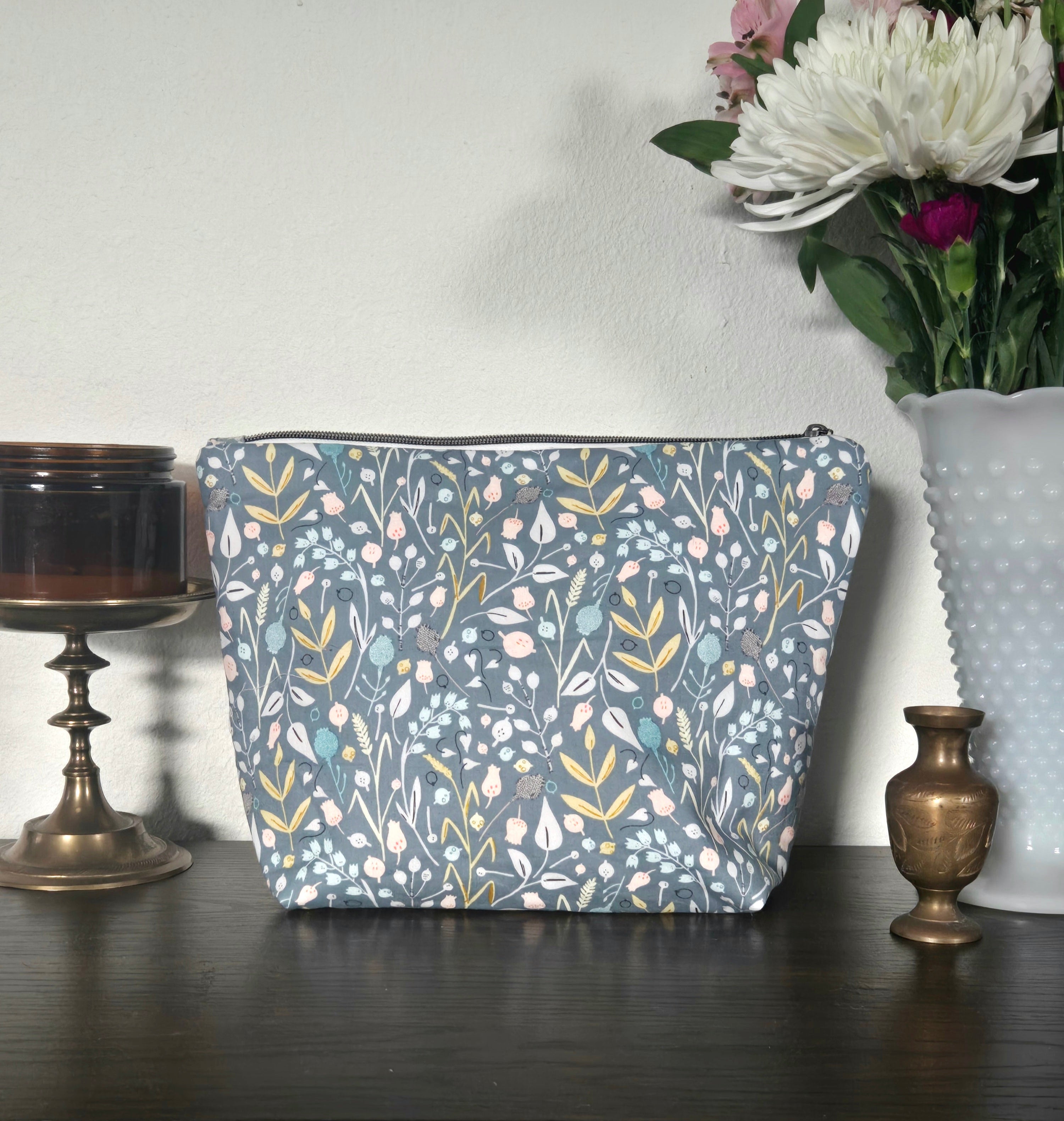 Floral-patterned pouch on a wooden surface with decorative items and flowers in the background.