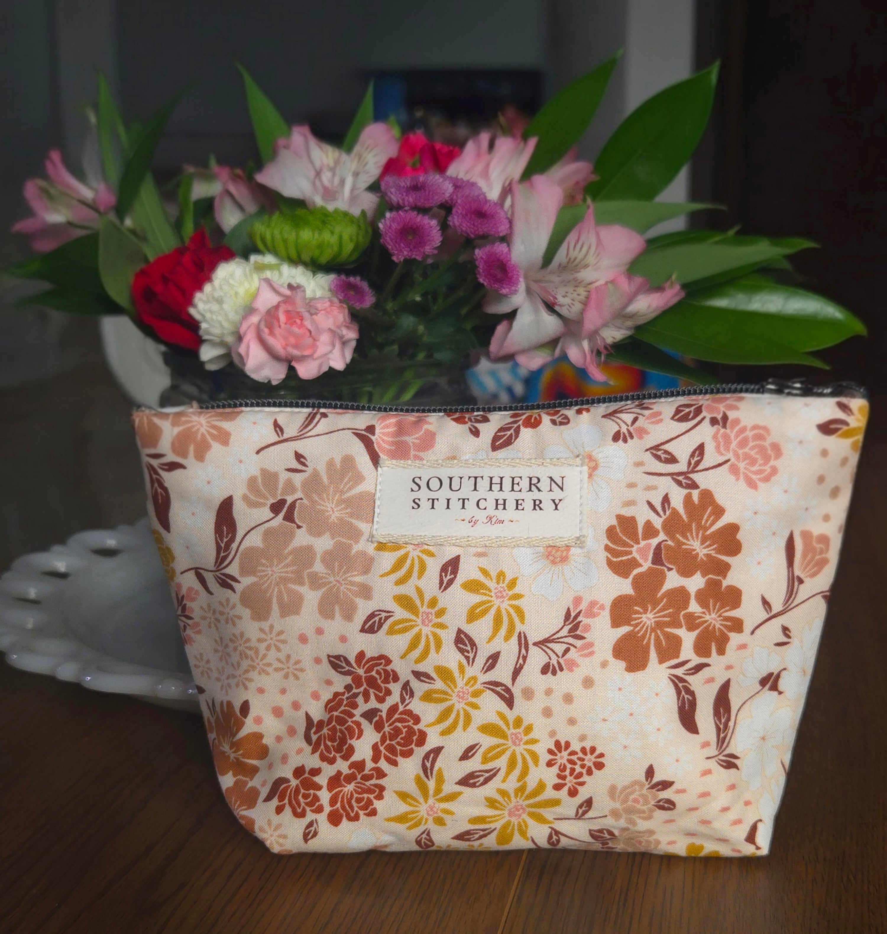 Floral-patterned bag with 'Southern Stitchery' label holding a bouquet of flowers.