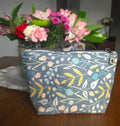 Floral-patterned pouch on a wooden surface with flowers in the background