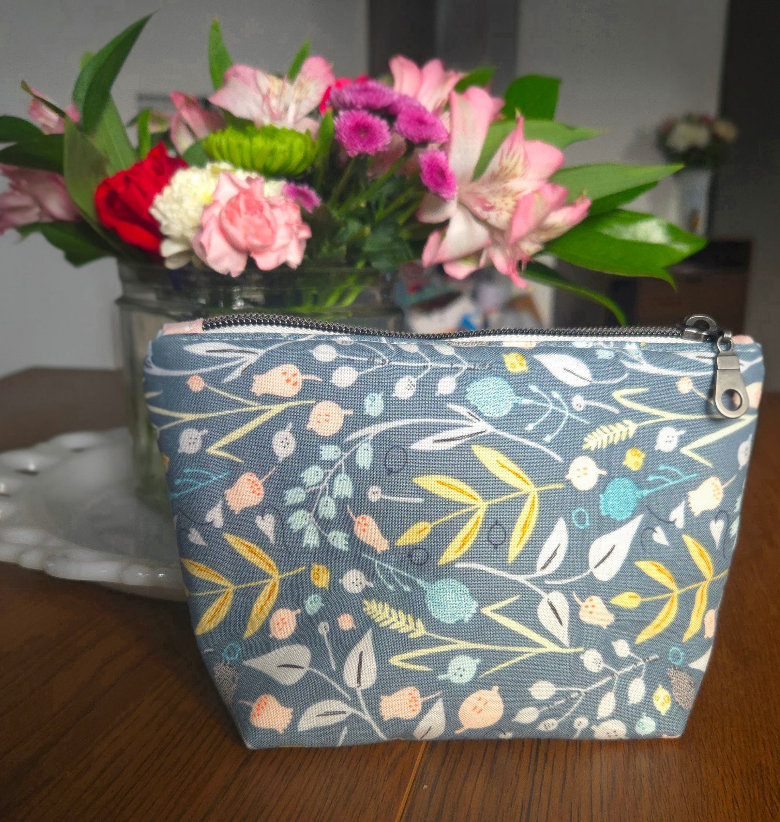 Floral-patterned pouch on a wooden surface with flowers in the background