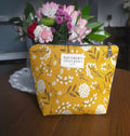Yellow floral-patterned bag with 'Southern Stitchery' label in front of a bouquet of flowers.